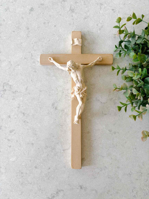 Wooden cross with a figurine of Jesus on a light gray background with a plant.