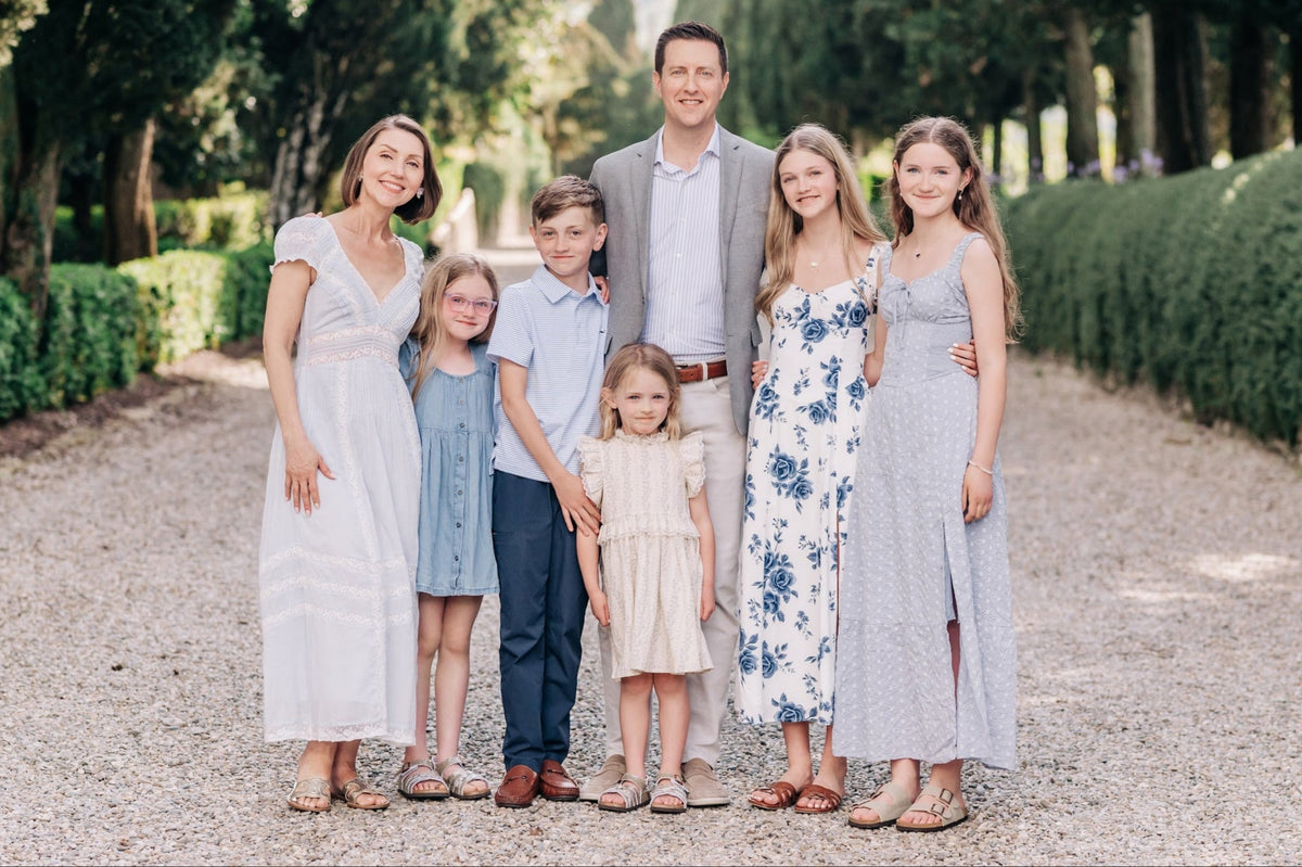 Family of seven standing on a gravel path with greenery in the background